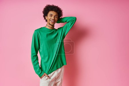 Téléchargez les photos : Un homme afro-américain joyeux et bouclé en chemise verte pose pour une photo sur un fond rose. - en image libre de droit