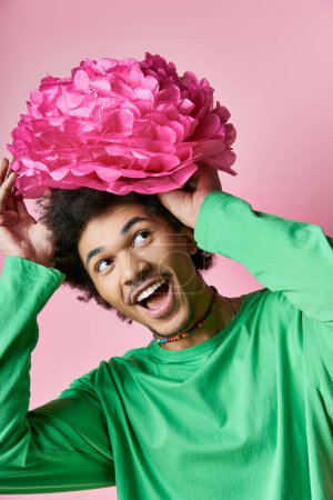Téléchargez les photos : Homme afro-américain joyeux aux cheveux bouclés portant des vêtements décontractés, affichant une émotion avec une fleur rose sur la tête. - en image libre de droit