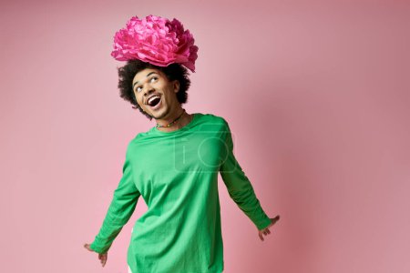 Foto de A joyful man with curly hair wearing a crown of pink flowers on her head against a vibrant backdrop. - Imagen libre de derechos