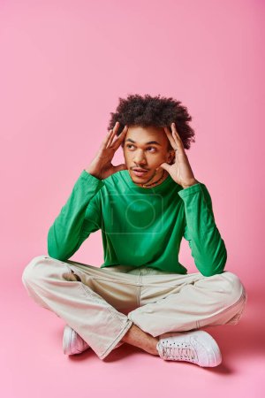 Young African American man sitting on pink floor with hands on head, deep in thought and emotion.