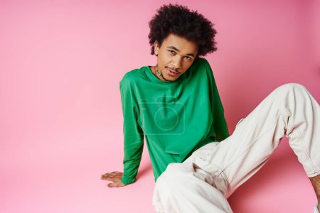 Foto de Joven hombre afroamericano con el pelo rizado con camisa verde casual y pantalones blancos sobre fondo rosa. - Imagen libre de derechos