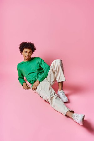 Photo for A cheerful, curly African American man in casual attire relaxes on a bright pink backdrop with exuberant emotion. - Royalty Free Image