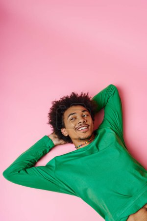 Photo for A cheerful curly African American man in a green shirt laying peacefully on a vivid pink background. - Royalty Free Image