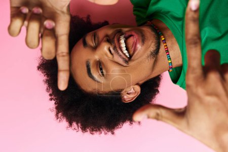 A curly African American man in casual wear looking through his framed hands on a pink background.