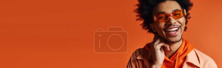 Ein junger Afroamerikaner in orangefarbenem Hemd und Sonnenbrille macht ein komisches Gesicht und zeigt seine lebhaften Emotionen.