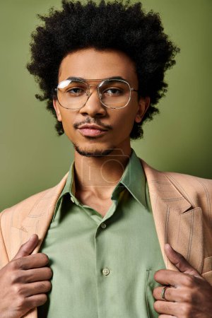 Foto de Un joven y elegante hombre afroamericano con el pelo rizado con atuendo de moda y gafas de sol sobre un fondo verde. - Imagen libre de derechos