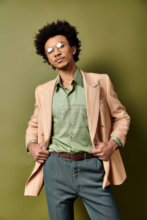 Stilvoller afroamerikanischer Mann in Anzug und Sonnenbrille posiert selbstbewusst vor grünem Hintergrund.