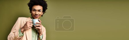 Photo for Young African American man with curly hair and trendy attire holding a cup in his right hand, wearing sunglasses on a green background. - Royalty Free Image