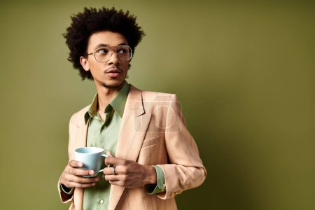 Stylish young African American man in trendy suit and sunglasses, savoring a cup of coffee against a green background.