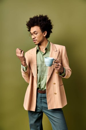 Ein junger, stylischer afroamerikanischer Mann mit lockigem Haar und Sonnenbrille hält eine Tasse Kaffee vor grünem Hintergrund.