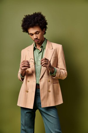 Stylish young African American man with curly hair wearing a tan jacket, green shirt, and sunglasses against a vibrant green background.