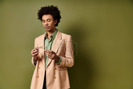 Ein stilvoller junger afroamerikanischer Mann im Anzug starrt intensiv auf seine Brille auf grünem Hintergrund.