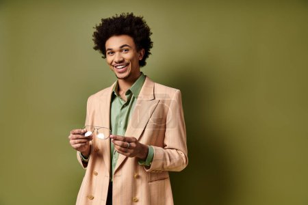 A stylish young African American man in a suit holding glasses against a vibrant green background.