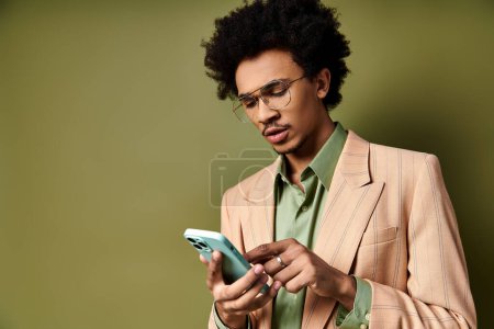 Foto de Un joven afroamericano con estilo en traje y gafas de sol, usando un teléfono celular sobre un fondo verde. - Imagen libre de derechos