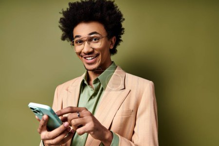 A young African American man in a stylish suit and sunglasses, confidently holding a smartphone against a green background.
