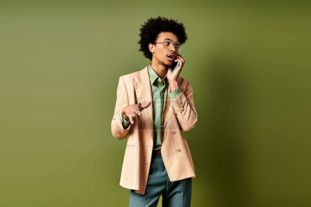 Photo for A stylish young African American man in a suit and sunglasses talking on a cell phone against a vibrant green background. - Royalty Free Image