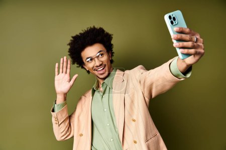 Foto de Young African American man in trendy suit and sunglasses taking a selfie with a cell phone on a green background. - Imagen libre de derechos