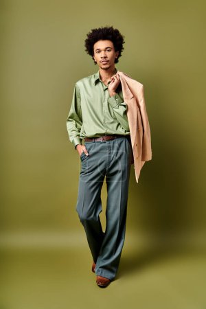 Photo for A fashionable young African American man with curly hair, trendy clothes standing confidently in front of a bright green wall. - Royalty Free Image