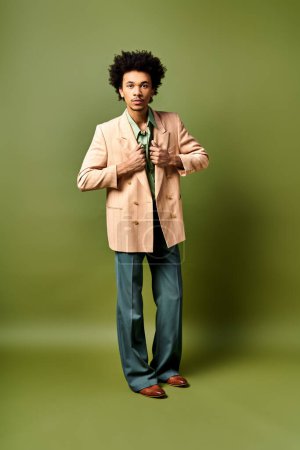 Un joven y elegante hombre afroamericano con el pelo rizado, con un traje de moda se para con confianza frente a un fondo verde vibrante.