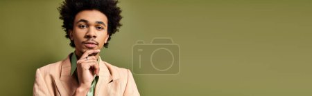 Foto de Un joven y elegante hombre afroamericano con el pelo rizado usando un traje, exudando confianza y sofisticación sobre un fondo verde. - Imagen libre de derechos