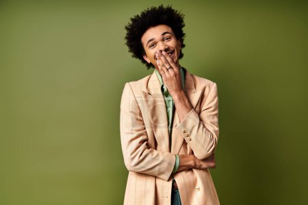 Foto de Un joven y elegante afroamericano vestido de moda de pie con las manos en la boca sobre un fondo verde. - Imagen libre de derechos
