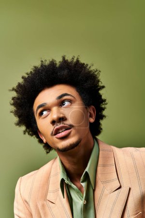 Ein stilvoller junger afroamerikanischer Mann mit lockigem Haar sieht vor grünem Hintergrund überrascht aus.