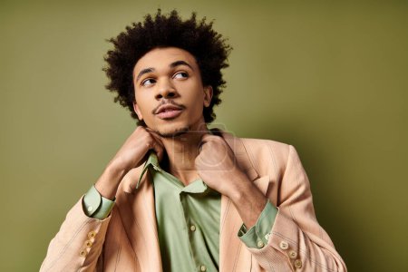 Photo for A stylish young African American man with curly hair, wearing a suit jacket and a green shirt, poses confidently against a green background. - Royalty Free Image