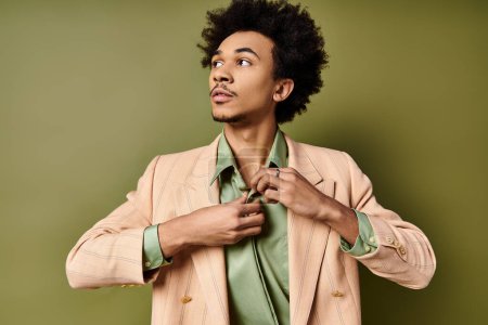 A stylish young African American man in a suit is skillfully buttoning shirt in front of a green background.