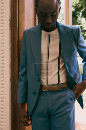 Handsome African American man in a blue suit standing stylishly next to a door.