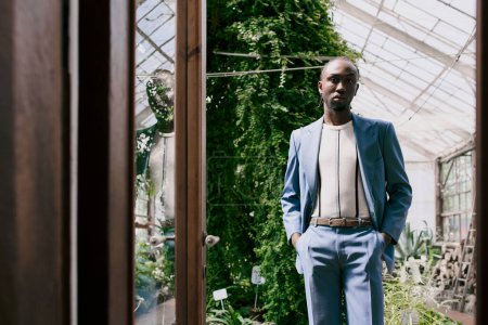 Sophisticated African American man in suit poses in vibrant greenhouse.