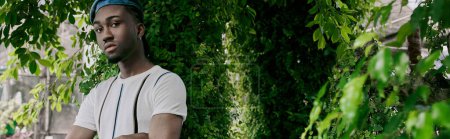 Téléchargez les photos : Un bel homme afro-américain au style dapper sophistiqué posant dans un jardin vert vif. - en image libre de droit