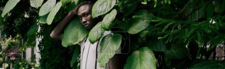 Foto de Hombre afroamericano guapo en estilo elegante rodeado de exuberante vegetación. - Imagen libre de derechos