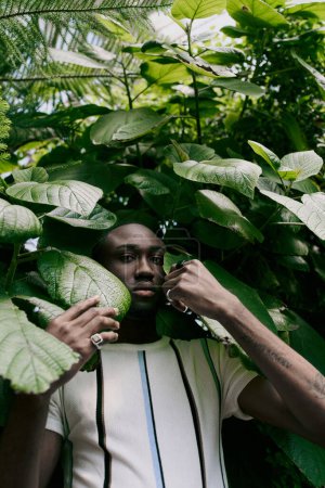 Téléchargez les photos : A handsome African American man in sophisticated dapper style poses in front of a lush green forest. - en image libre de droit