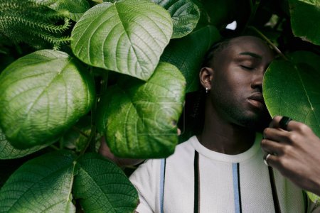 Handsome African American man posing stylishly next to a lush green plant in a vivid garden setting.