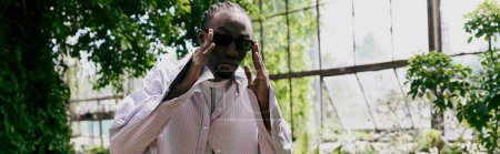 Téléchargez les photos : A sophisticated African American man in a white shirt and tie walking through a forest. - en image libre de droit