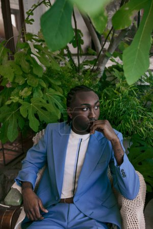 Handsome African American man in stylish blue suit sitting gracefully in lush green garden.