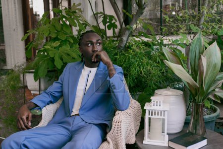 Handsome African American man in a blue suit, sitting on a chair in a vibrant green garden.