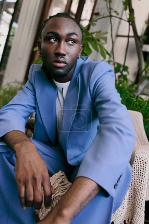 Stylish African American man in blue suit sitting on a chair in a vibrant green garden.