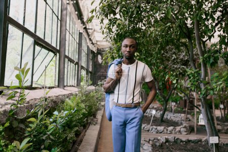 Sophisticated African American man poses fashionably in a lush greenhouse garden.