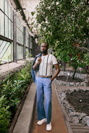 Un homme afro-américain sophistiqué debout en toute confiance devant un bâtiment coloré dans un jardin luxuriant.