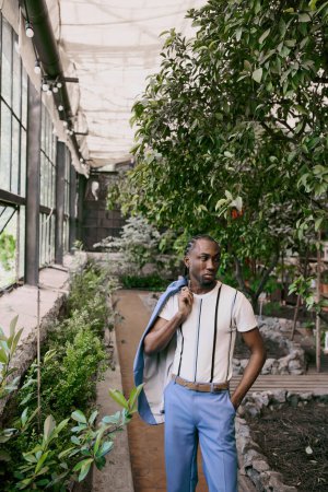 Téléchargez les photos : Beau Afro-Américain en tenue sophistiquée pose dans un jardin vert vif. - en image libre de droit