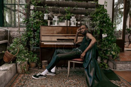 Un bel homme en tenue sophistiquée est assis à côté d'un piano à queue dans un jardin verdoyant animé.