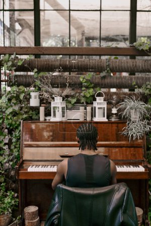 A man sits at a piano, playing in greenhouse.