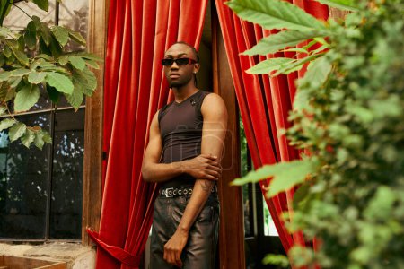 Téléchargez les photos : Un bel homme afro-américain se tient en confiance devant un riche rideau rouge. - en image libre de droit