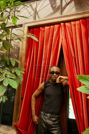 Un Afro-Américain sophistiqué se tient en confiance devant un rideau rouge.