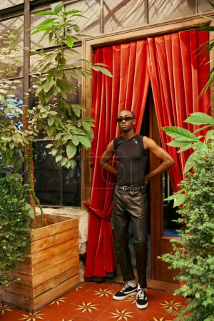 Un bel homme afro-américain se tient en confiance devant un rideau rouge vibrant.