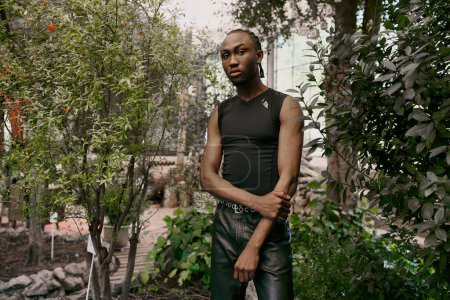 Téléchargez les photos : Un bel homme afro-américain avec un style sophistiqué dapper debout en toute confiance dans un jardin vert animé. - en image libre de droit