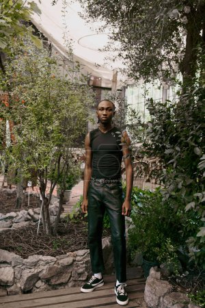 Ein gutaussehender afroamerikanischer Mann mit elegantem Stil steht in einem lebhaften grünen Garten.