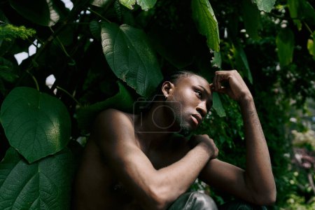 Foto de Un hombre sin camisa con estilo elegante posando pacíficamente en un jardín verde vívido. - Imagen libre de derechos