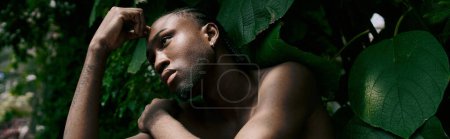 Foto de Un hombre afroamericano sin camisa con estilo elegante en un exuberante jardín verde. - Imagen libre de derechos